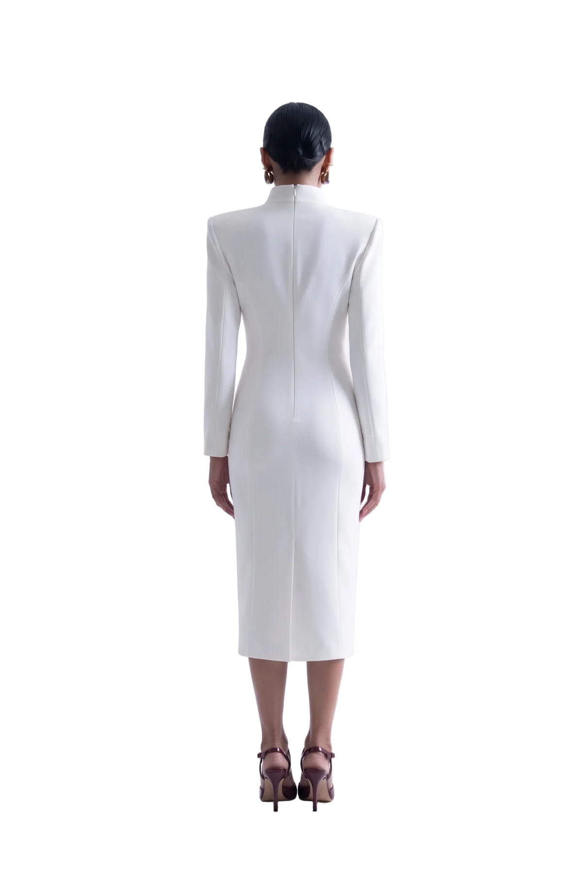 A model viewed from the back wearing a white long-sleeve midi dress with structured shoulders and a high mock neck, paired with dark brown strappy heels against a seamless white studio background.